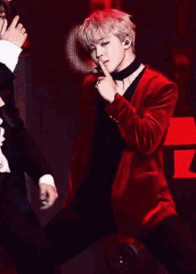 a man in a red jacket and choker is holding his finger to his lips