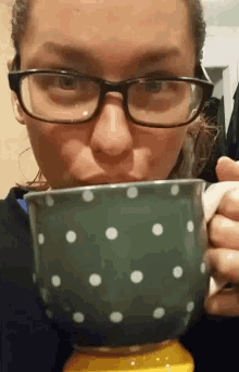 a woman wearing glasses is drinking from a green polka dot mug