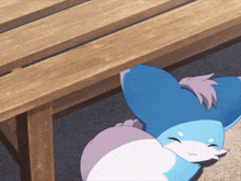 a blue and white cartoon character laying under a wooden table