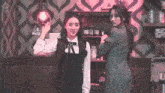 two women are standing next to each other in a room . one of the women is holding a light bulb .