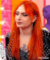 a woman with red hair and hoop earrings is wearing a black jacket with spikes .