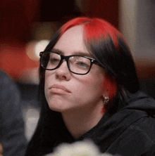 a woman with red and black hair wearing glasses and earrings