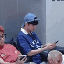 a man in a blue hat is sitting on a couch looking at his cell phone .