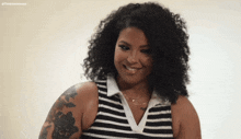 a woman with curly hair wearing a black and white striped shirt is smiling