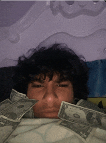 a man is laying on a bed with a bunch of money on his face