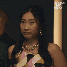 a woman wearing a necklace and earrings with the words " you 're my hero " behind her