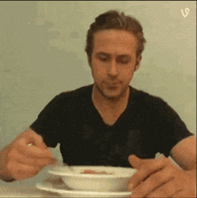 a man in a black shirt is eating from a bowl with a spoon
