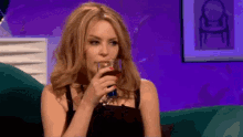 a woman is drinking from a glass while sitting on a couch .