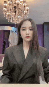 a woman in a suit stands in front of a chandelier in a room