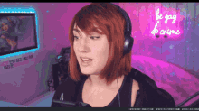 a woman wearing headphones stands in front of a neon sign that says be gay be crime