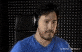 a man wearing headphones and a blue shirt is making a funny face with his mouth open .