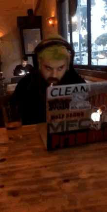 a man with green hair is sitting at a table with a laptop that says clean