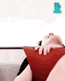 a person is laying on a couch holding a red pillow with their head on it .