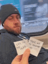 a man sitting on a train holding a piece of paper that says take me to dinner