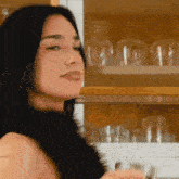 a woman is holding a glass in front of a shelf of glasses