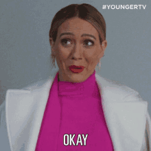 a woman wearing a pink sweater and white jacket says okay