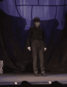 a man in a black suit is standing on a stage in front of a purple curtain
