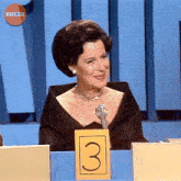 a woman sitting at a table with a yellow sign that has the number 3 on it