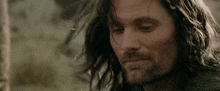 a man with long hair and a beard is looking down and smiling .