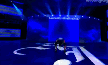 a person is doing a handstand on a stage with a blue background and the words the next big thing on the bottom .