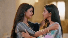 two women are hugging each other and looking at each other in a room .