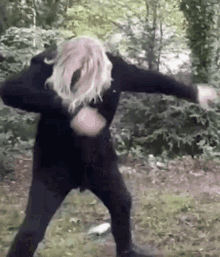 a woman in a black jacket and black pants is doing a dab in the grass .
