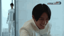 a man in a white jacket is smiling in front of a logo for kamen rider