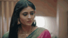 a close up of a woman wearing a pink and green saree and earrings