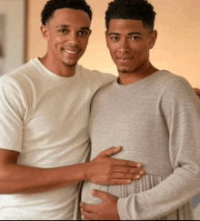 two men standing next to each other with one holding the belly of a pregnant woman