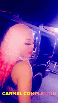 a woman with pink hair is standing in front of a car with the words carmel complexion on the bottom right