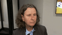 a woman with long curly hair wearing a suit and blue shirt