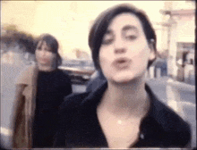 two women are standing next to each other on a street and one of them is talking .