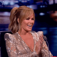 a woman in a sequined dress is smiling and clapping in front of a microphone