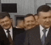 a group of men in suits and ties are standing in a room .