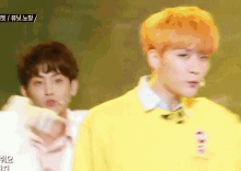 two young men are standing next to each other on a stage and one of them has orange hair .