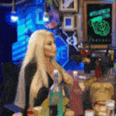 a woman with blonde hair is sitting at a table with bottles of alcohol