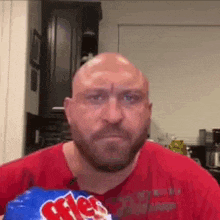a bald man with a beard is holding a bag of m & ms .