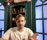 a man in a white shirt stands in front of a bookshelf