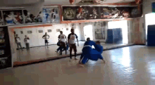 a group of people are practicing martial arts in a gym while a referee watches .