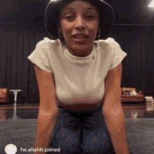 a woman wearing a hat and a white t-shirt is kneeling down