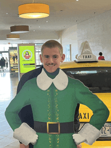 a boy in a green elf costume stands in front of a taxi
