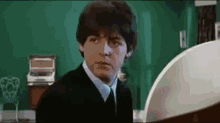 a man in a suit and tie is standing in front of a piano .