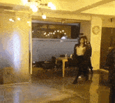 a woman walking in a room with a table and chairs and a clock on the wall