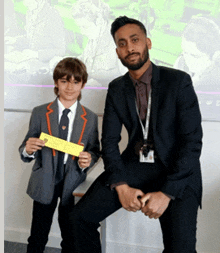 a man in a suit sits next to a boy in a school uniform holding a piece of paper