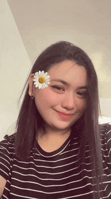 a woman is wearing a striped shirt and a daisy in her hair .