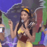 a woman in a yellow dress is holding a trophy in front of a microphone .