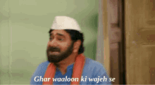 a man with a beard wearing a white hat and an orange scarf says ghar waaloon ki wajah se