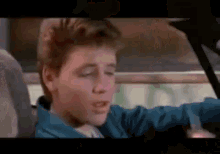 a young boy in a blue jacket is sitting in the back seat of a car with his eyes closed .