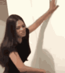a woman in a black shirt is sitting in front of a white wall with her arm outstretched .