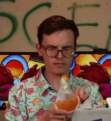 a man wearing glasses is holding a bottle of orange juice in front of a wall with the letter s on it